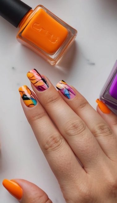 Bright orange nails paired with colorful painted accents, mimicking brushstroke patterns for a bold, expressive look.