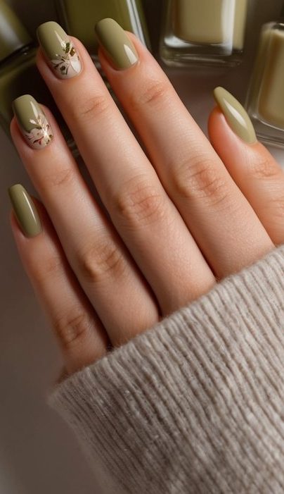 Trendy September nail design featuring sage green and nude polish with delicate floral nail art against autumn leaf backdrop