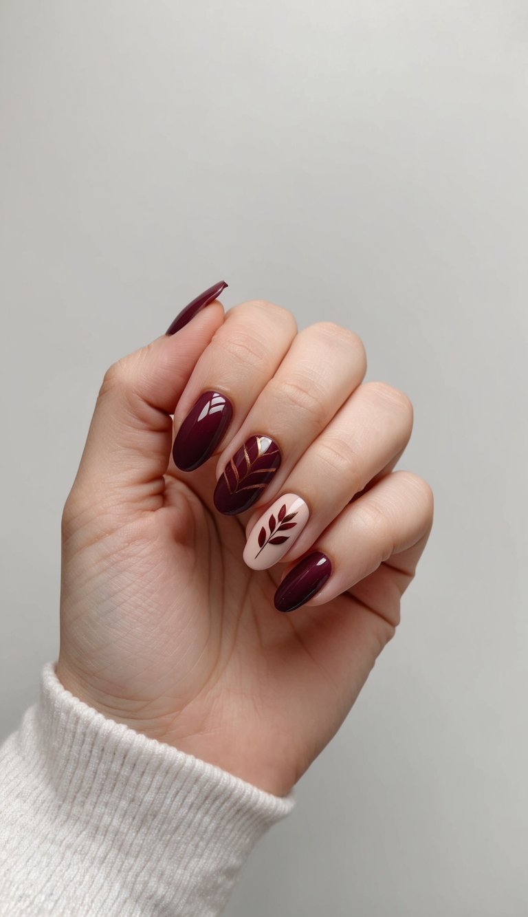 Sophisticated almond-shaped nails displaying deep burgundy and nude polish with intricate gold leaf silhouette designs against minimal background