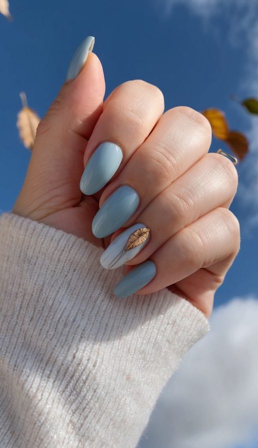 Romantic sky blue manicure featuring delicate golden leaf artwork captured against autumn sky with naturally falling leaves creating whimsical atmosphere