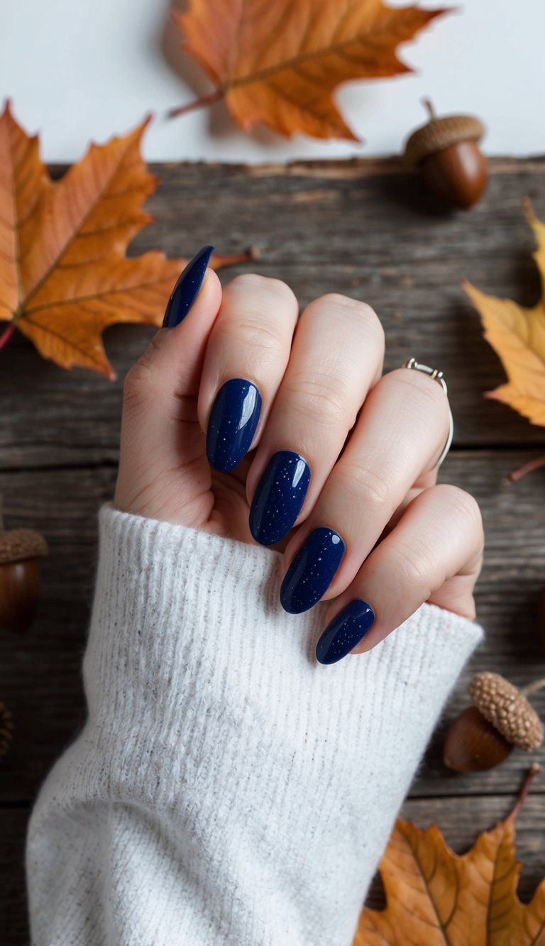 Cozy midnight blue nail design featuring delicate glitter accents styled with warm autumn leaves and natural elements on rustic wooden surface