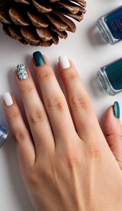 Hand with green, white, and dotted accent nails, inspired by winter pine and snowfall for a crisp seasonal manicure.