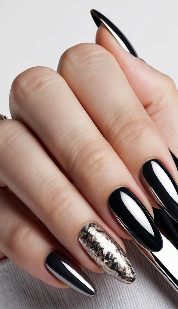 Hand with black chrome stiletto nails and one silver textured accent nail posed next to black styling tool on gray fabric.
