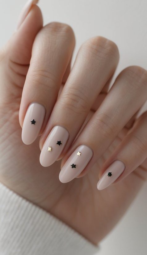 Soft nude nails adorned with tiny black and gold star accents, adding a delicate celestial twist to plain nail art.