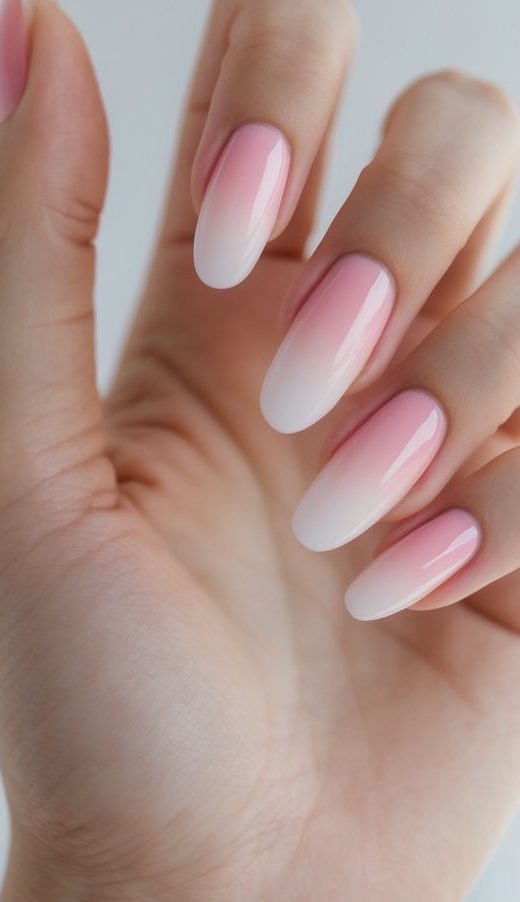 Close-up of one hand with ombre pink to clear gradient nails against a white background.