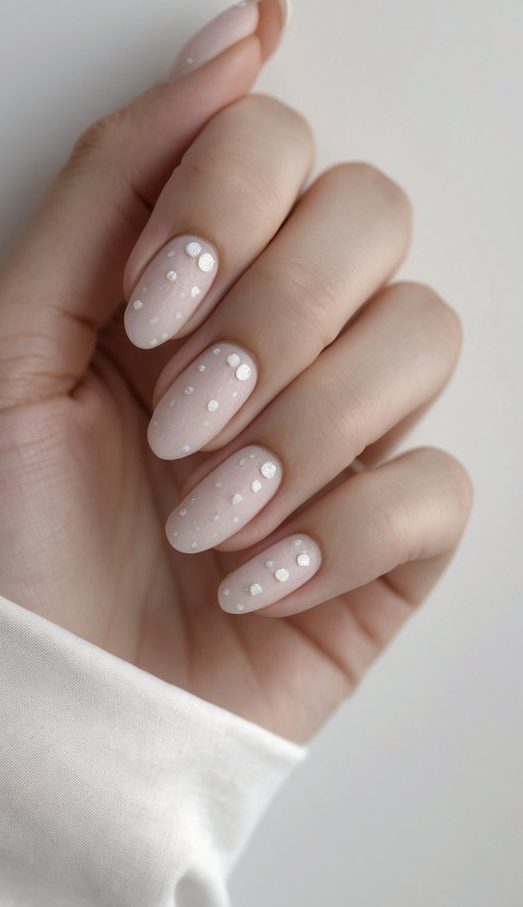 Close-up of one hand showing nails with simple silver dot nail art on a white background.