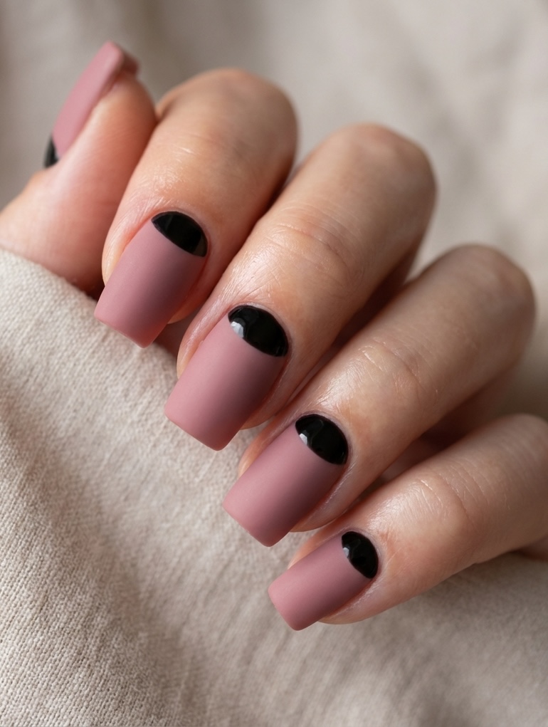 Hand with square-shaped nails showing a reverse French nail art idea in matte mauve with glossy black moon detailing at the nail base.