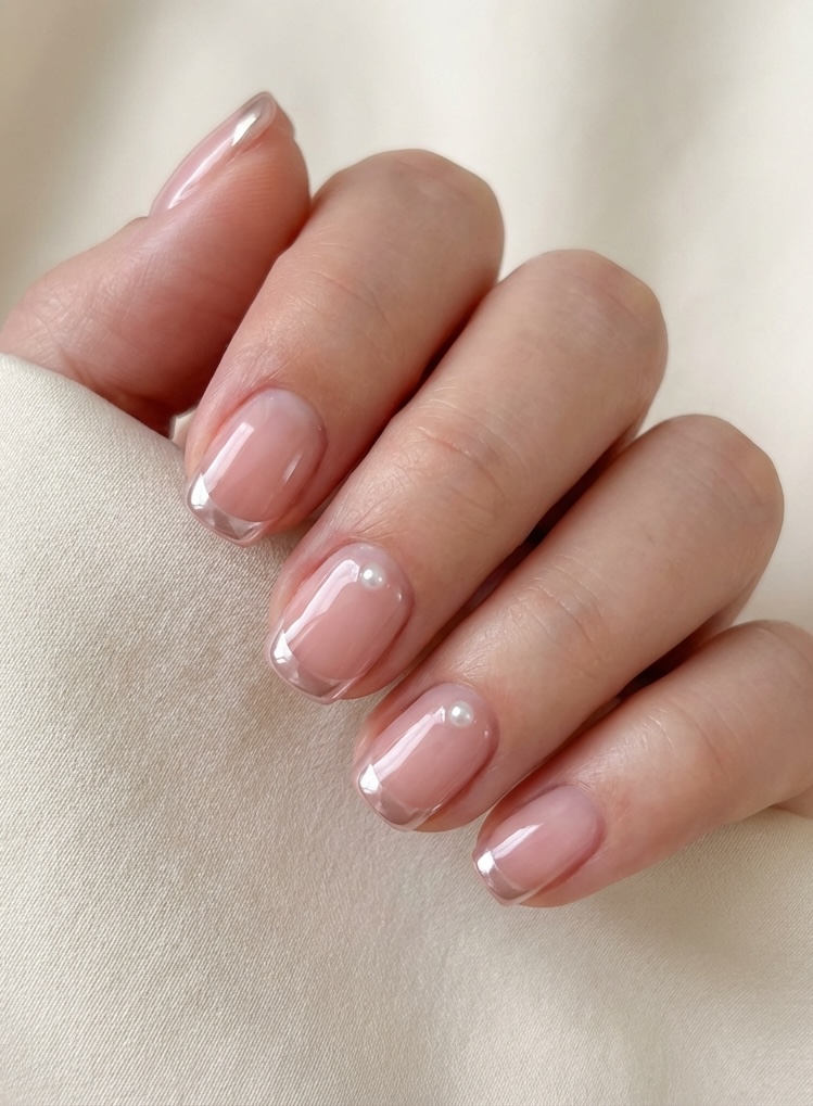 Editorial-style image of fingers featuring a glazed nail art idea with crystal-clear tips, soft pink base, and small pearl embellishments.