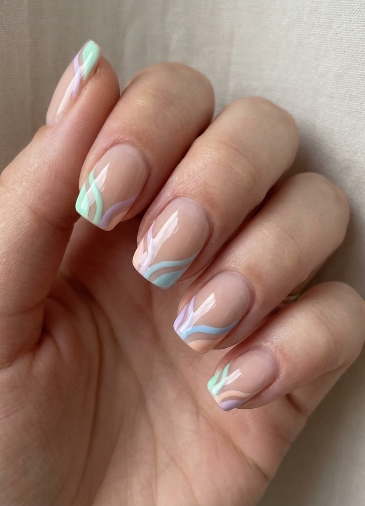 Close-up of a hand with short square nails featuring a short nail art idea using nude polish with flowing pastel lines in mint, lilac, and soft blue.