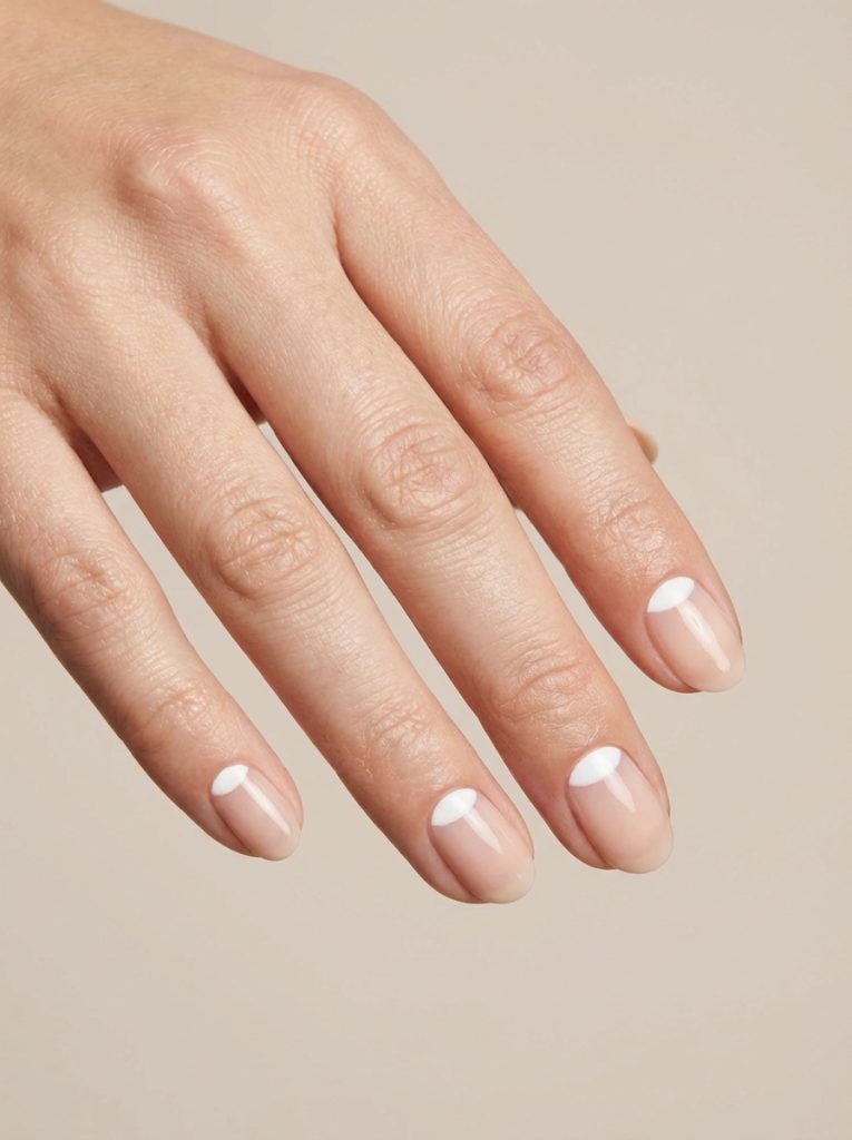 Close-up view of a hand showcasing the reverse French nail art idea with neat white half-moon shapes contrasting against subtle, sheer pink nail beds.
