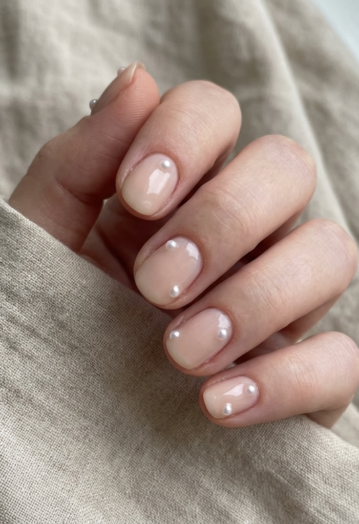 Short nail art idea on natural nails, painted in translucent nude polish and decorated with tiny pearl beads on each fingertip.