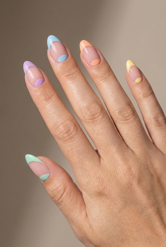 Almond-shaped nails in a reverse French nail art idea with bright pastel half-moons and tips over a sheer nude background, hand raised against neutral backdrop.