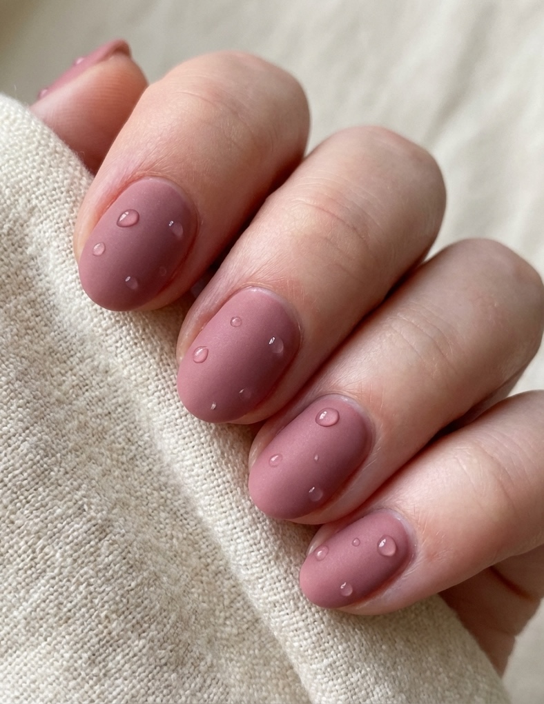 Close-up of a dusty rose nail art idea where a velvety pink-mauve base is paired with small, raised clear beads resembling tiny water drops on each nail.