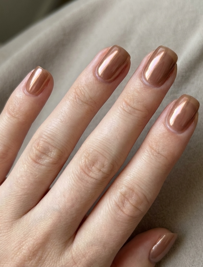 Close-up of neatly manicured fingers featuring a glazed nail art idea in high-shine copper chrome on short square nails.