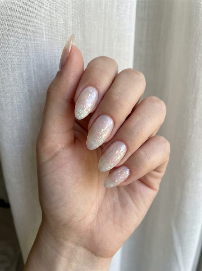 Close-up of almond-shaped nails styled in a glazed nail art idea, featuring a soft pink base and luminous flake details catching the light.