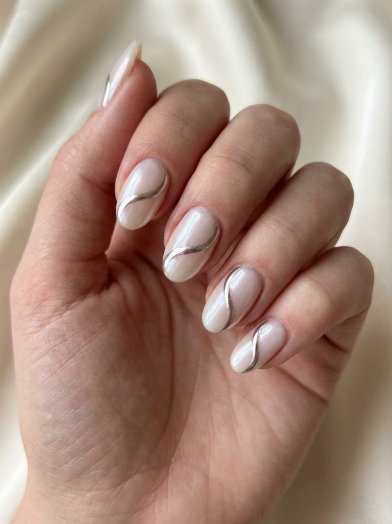 Hand with soft-glazed nude nails, each detailed with a single flowing silver chrome line for a modern glazed nail art idea.