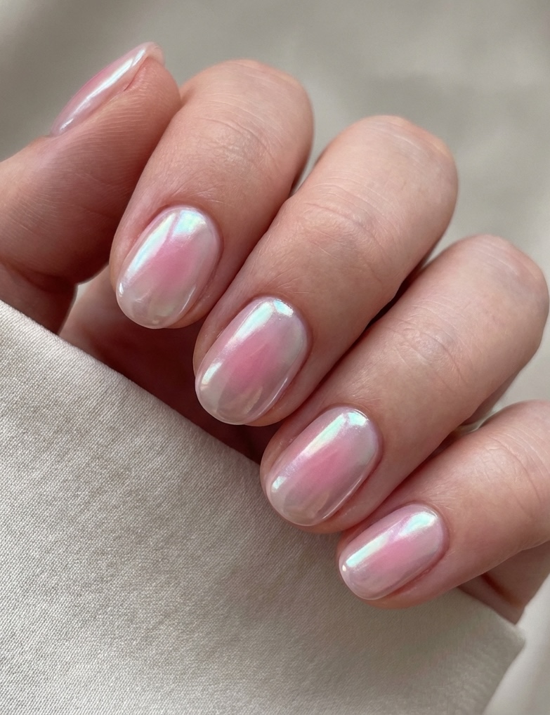 Close-up of fingers featuring a glazed nail art idea with pink jelly polish and reflective, opalescent highlights on natural-length nails.