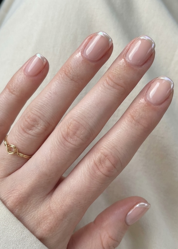 Hand with short glossy nails styled in a glazed nail art idea, finished with thin, glistening pearl French tips for a fresh twist.