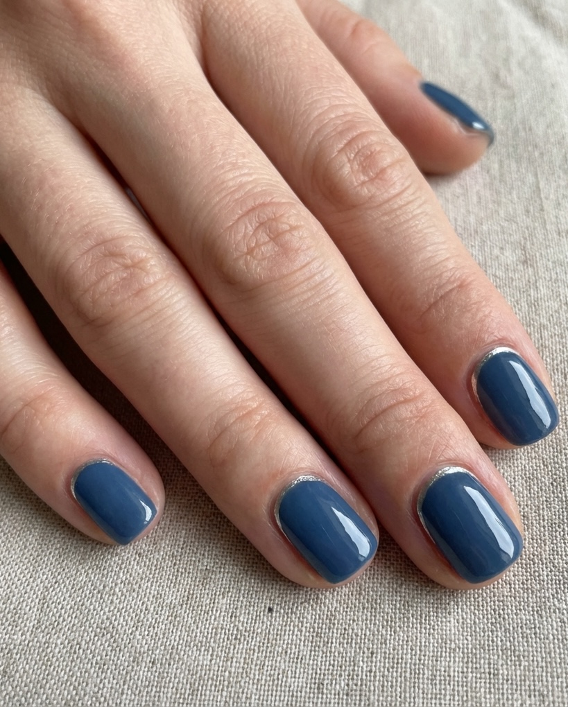 Fingers with short, square-shaped nails painted in deep blue and outlined with fine silver half-moons in a reverse French nail art idea.