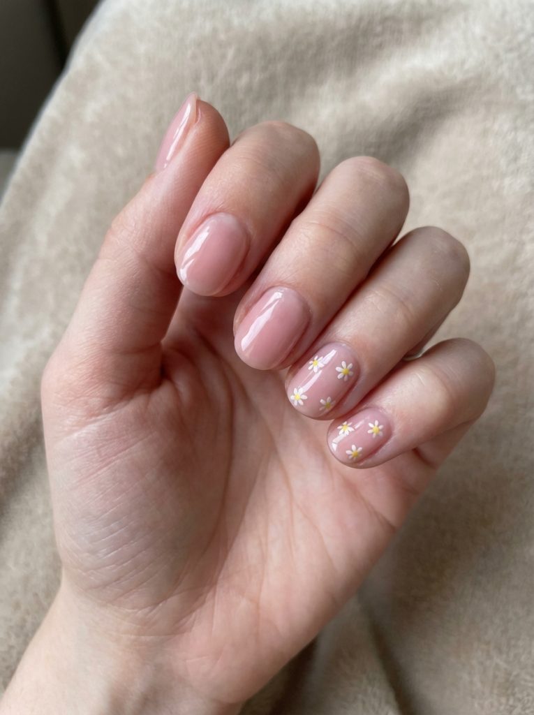 Glossy blush nails shown in a glazed nail art idea, featuring miniature daisy designs on select fingers for a subtle floral highlight.