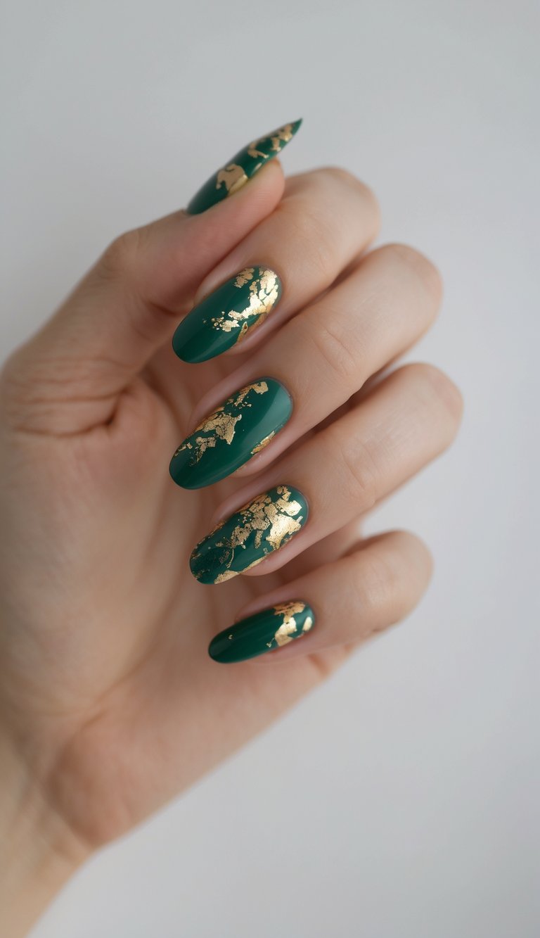 A hand with almond-shaped emerald green nails decorated with scattered gold foil flakes, showcasing a green and gold nail art idea that blends natural richness with metallic elegance.