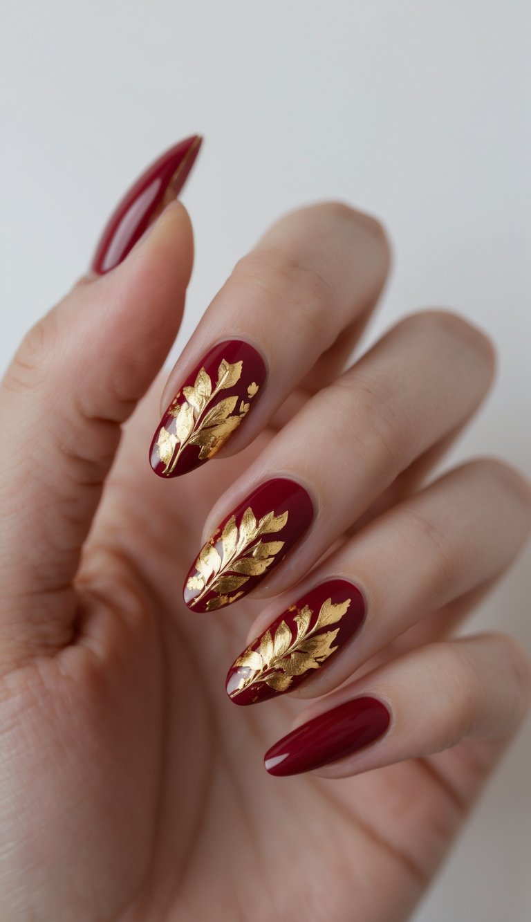 Hand with deep red glossy nails featuring bold gold foil leaves, styled as an elegant Chinese New Year nail art idea.