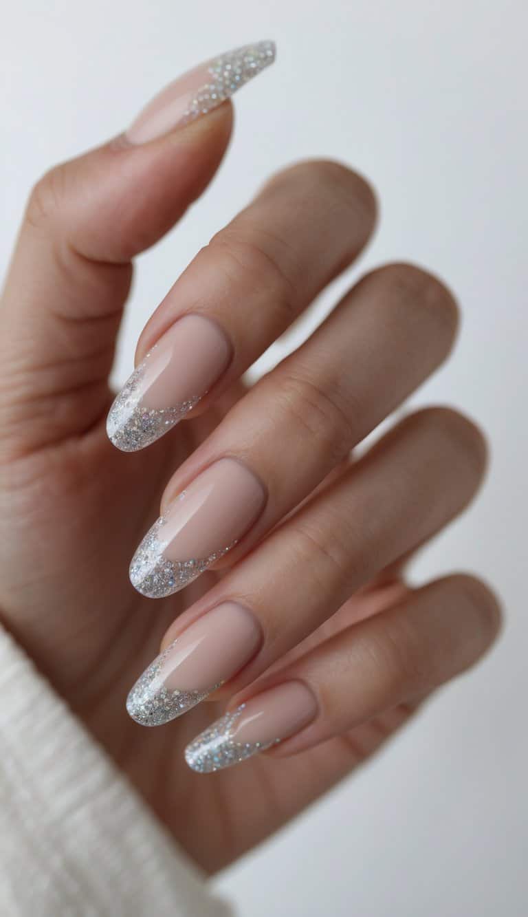 Close-up of a hand showing almond-shaped blush nude nails finished with fine silver glitter French tips, presenting a minimal graduation nail art idea with a soft glossy finish
