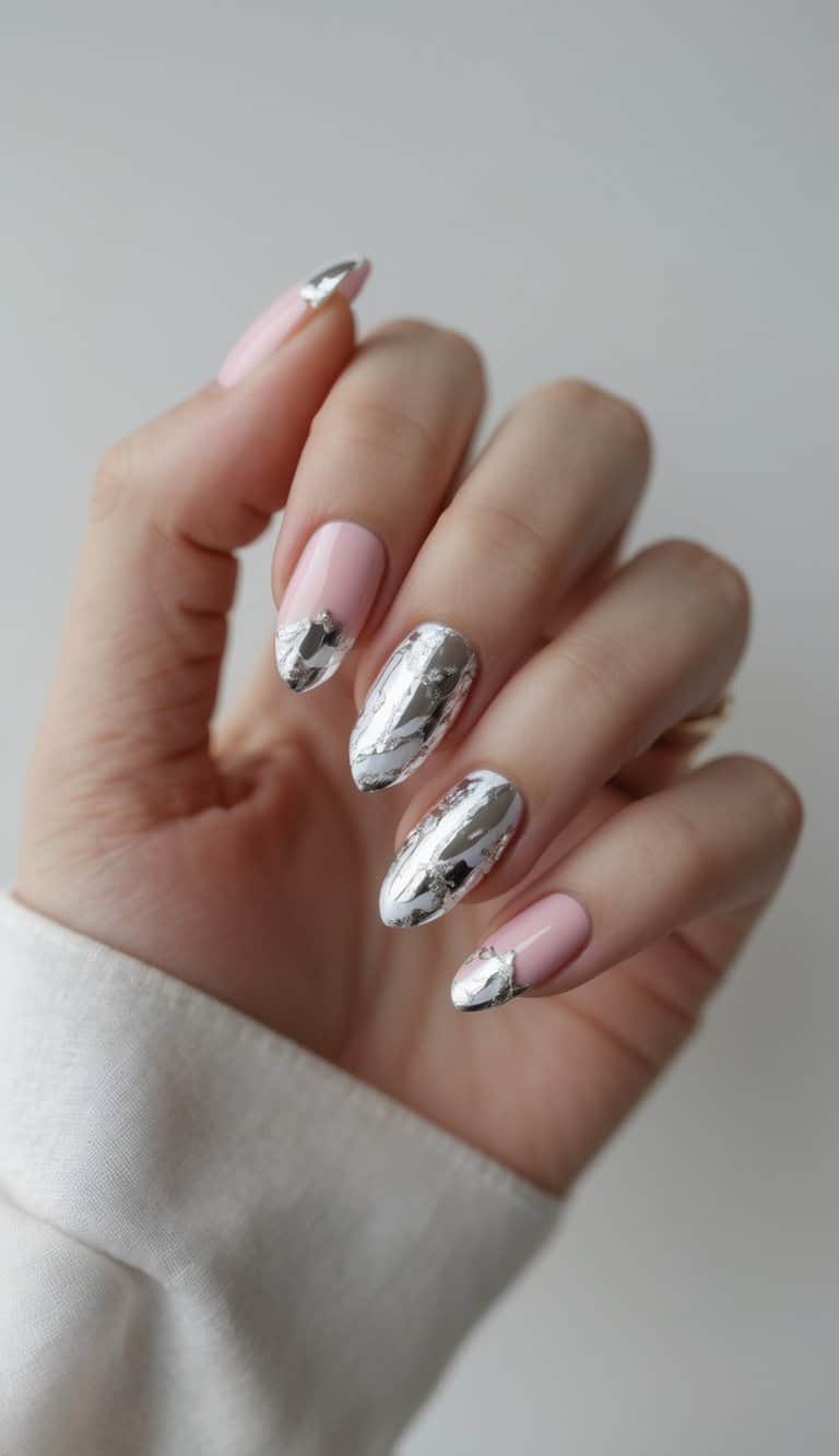 Close-up of a hand with blush pink nails, some fully covered in silver foil and others with chrome tips—elegant and bold february nail art ideas.