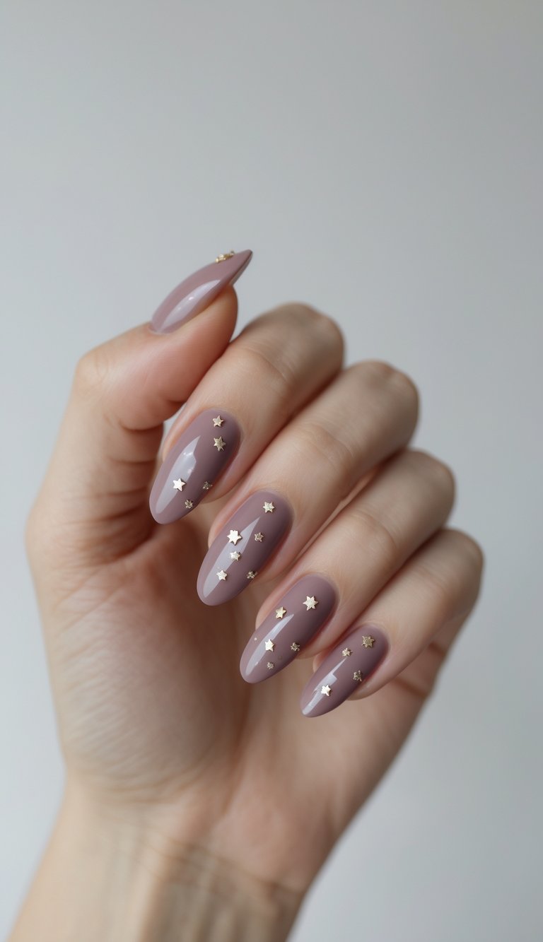 Hand posed against a neutral background showing oval mauve nails with glossy shine, topped with metallic gold stars for a subtle yet eye-catching April nail art idea.