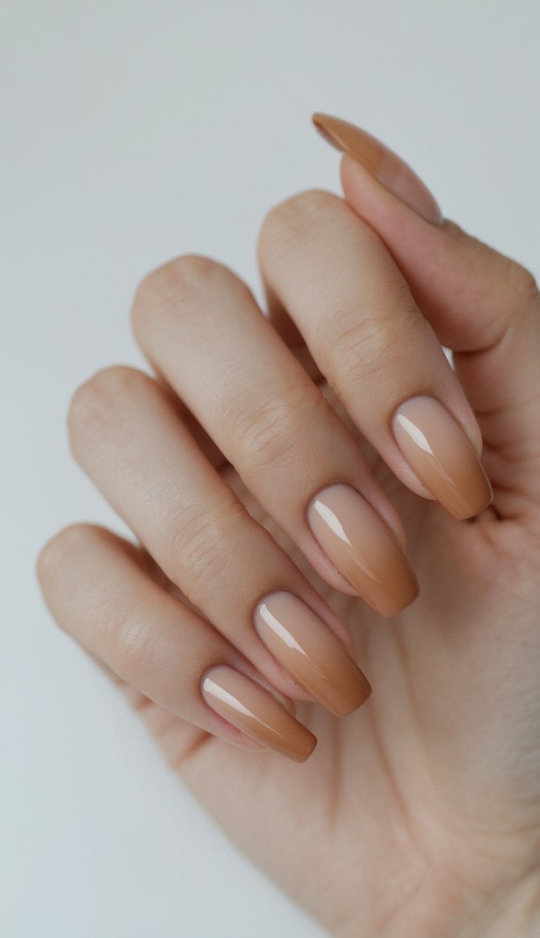 Feminine hand with glossy ombré nails in beige and caramel shades, highlighting a clean girl nail art idea with warm gradient tones and subtle shine