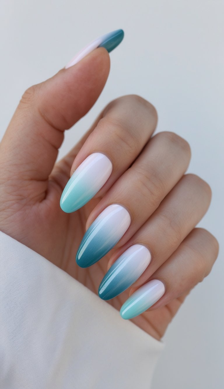 A hand with elongated almond nails painted in a playful DIY nail art idea blending white into turquoise and ocean blue in a smooth gradient finish.
