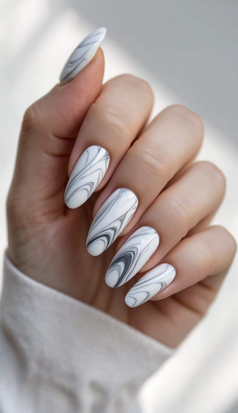 A hand displays long almond nails painted with white polish and realistic marble-like grey and black veins in a minimalist DIY nail art idea.