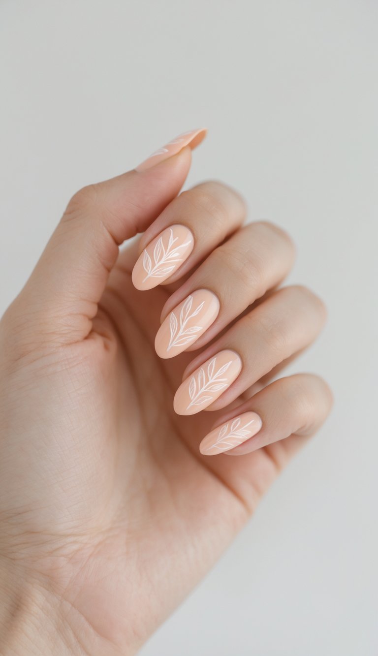 A hand displays almond-shaped peach nails, each painted with fine white leafy lines, showing a soft and clean delicate nail art idea.