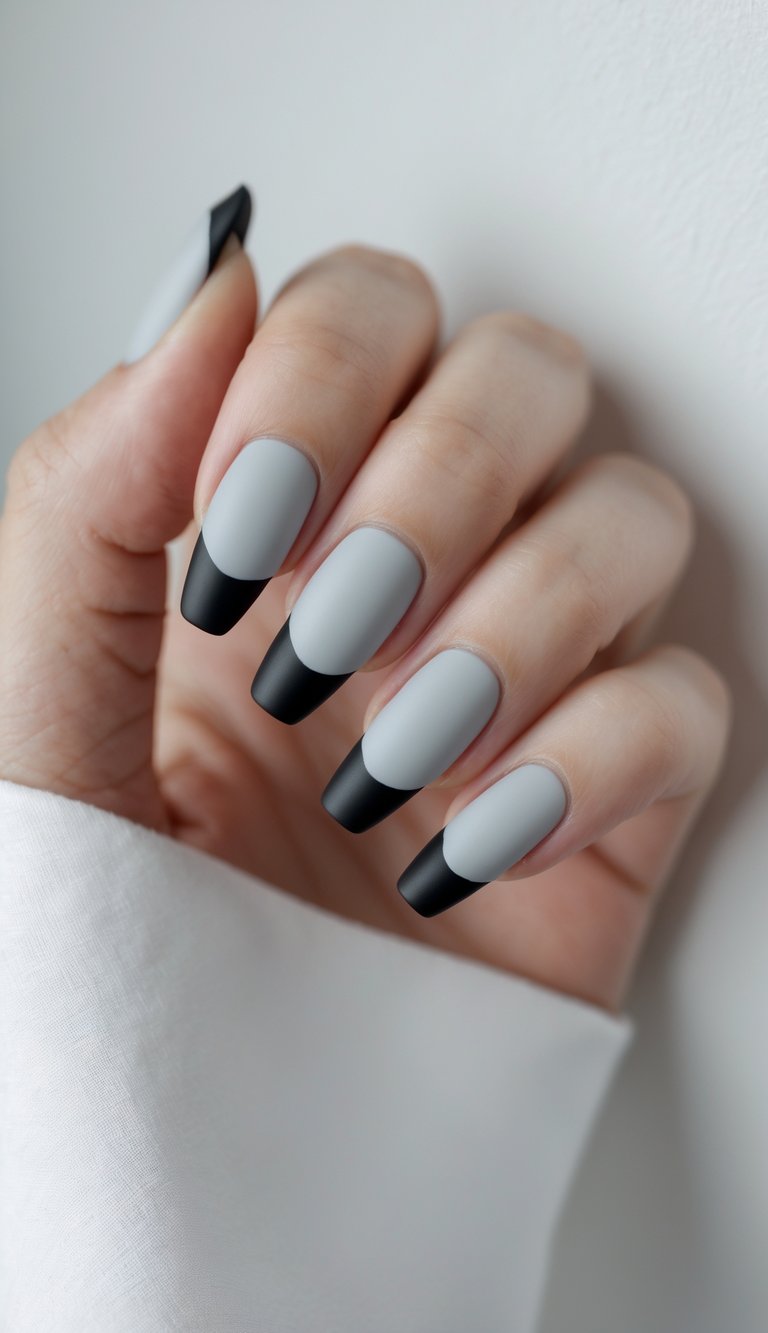 Close-up of one hand with light grey nails and matte black tips against a white background.