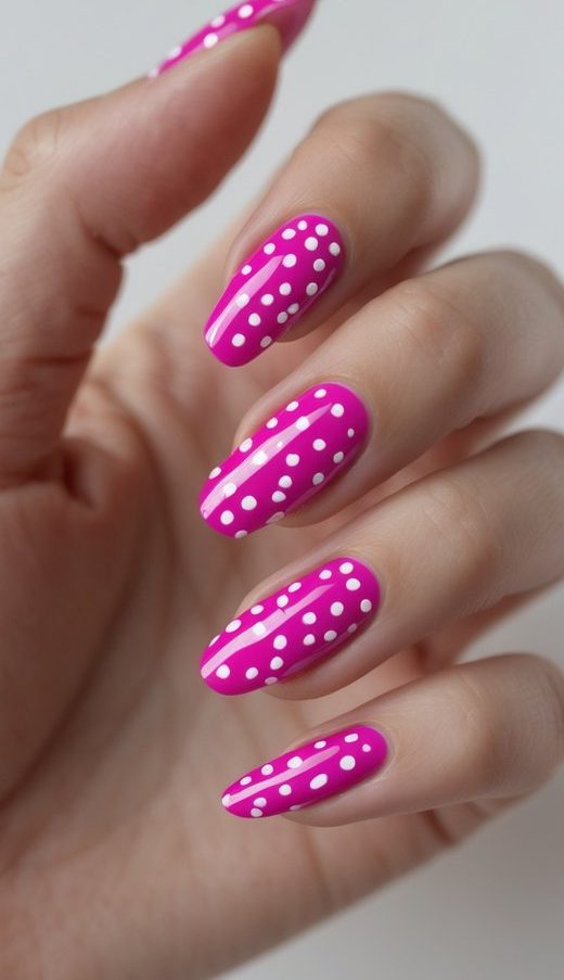 A hand with a fuchsia nail art idea featuring bold white polka dots on shiny hot pink polish, capturing a lively retro-inspired manicure.