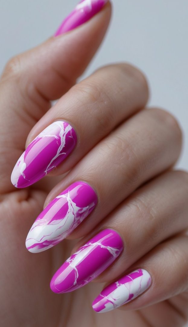 Close-up of a hand with almond-shaped nails showcasing a fuchsia nail art idea with sharp white marble-like veining flowing across a glossy hot pink base.
