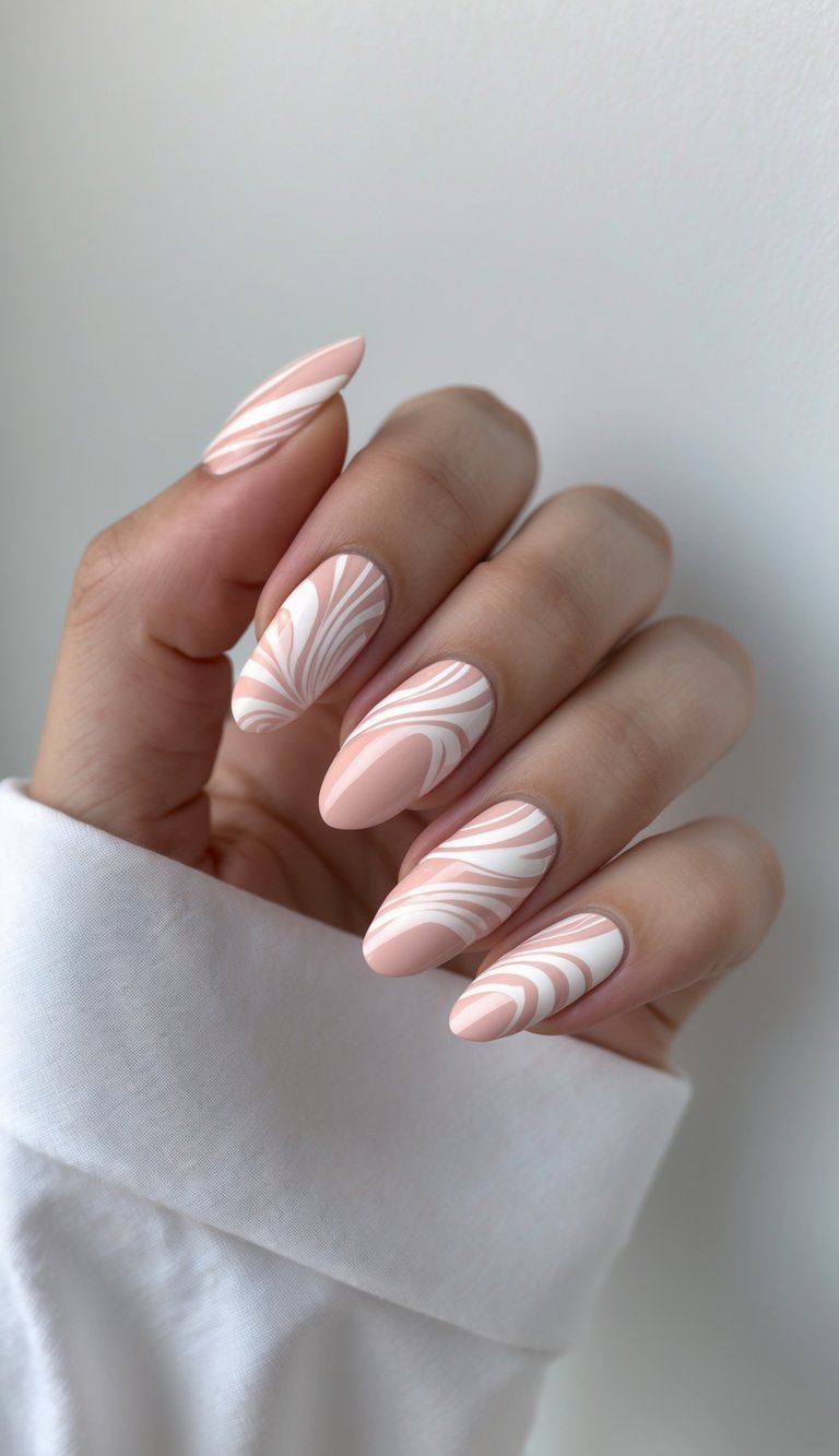 Elegant hand displays a blush nail art idea with smooth, almond-shaped nails painted in a matte base, overlaid with fluid white and pink swirl designs that mimic delicate brushwork.