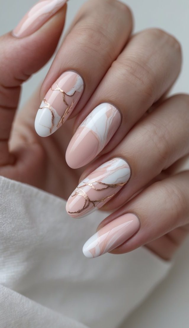 Hand with almond-shaped nails showcasing a blush nail art idea where creamy pink and white swirls are veined with fine metallic gold lines, mimicking natural marble patterns.