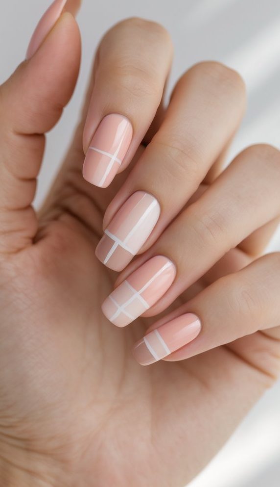 Close-up of a hand wearing a blush nail art idea with squared nails, painted in glossy nude blush and accented with crisp white striping for a clean, modern finish.