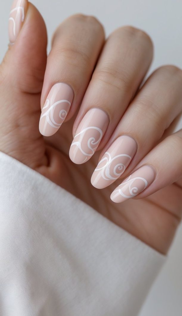 Blush nail art idea shown on long, rounded nails with a nude base and soft, white swirl accents that wrap gracefully across each fingertip in a clean, fluid style.