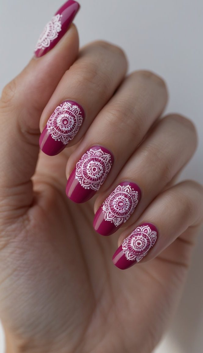 Angled view of a hand displaying a raspberry nail art idea with deep magenta nails, each accented by crisp white mandala-style linework and a smooth glossy surface.