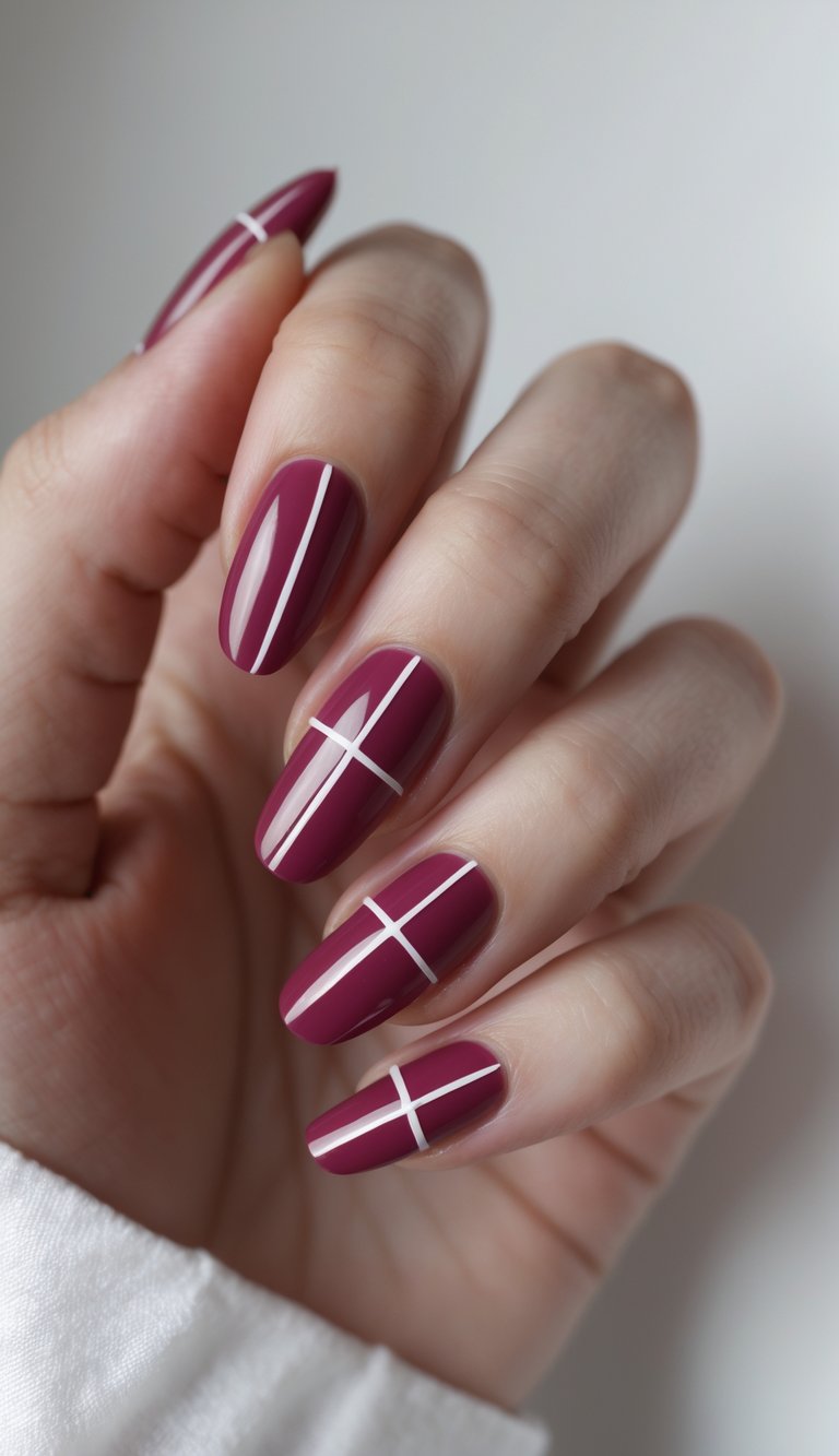 The image shows a neutral background with a hand wearing almond-shaped nails painted in glossy raspberry, detailed with minimal white linear accents arranged in clean geometric patterns.