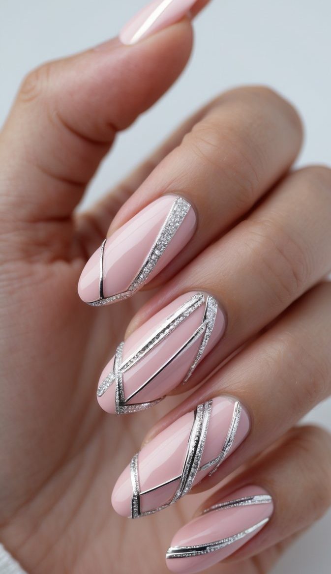 Seen from above, a manicured hand displays a pink and silver nail art idea with blush-pink nails crossed by thin silver metallic and glitter-lined accents.