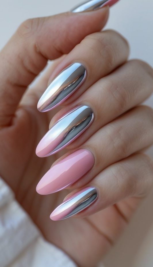 Captured in soft lighting, a hand reveals long almond nails styled in a pink and silver nail art idea, highlighting pastel pink bases alongside reflective silver chrome nails.