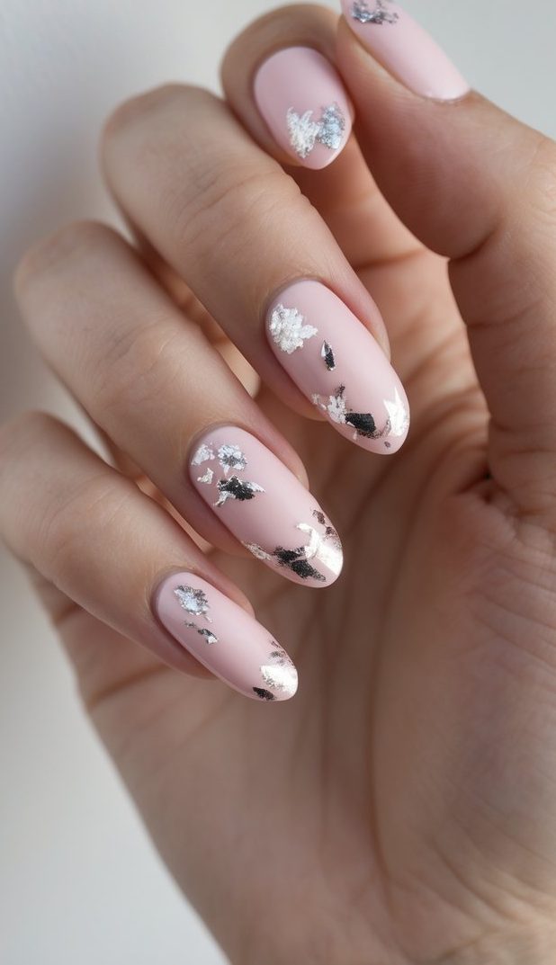 A softly lit image captures a manicured hand showing a pink and silver nail art idea, where smooth pink nails are accented by organic silver foil pieces placed unevenly.