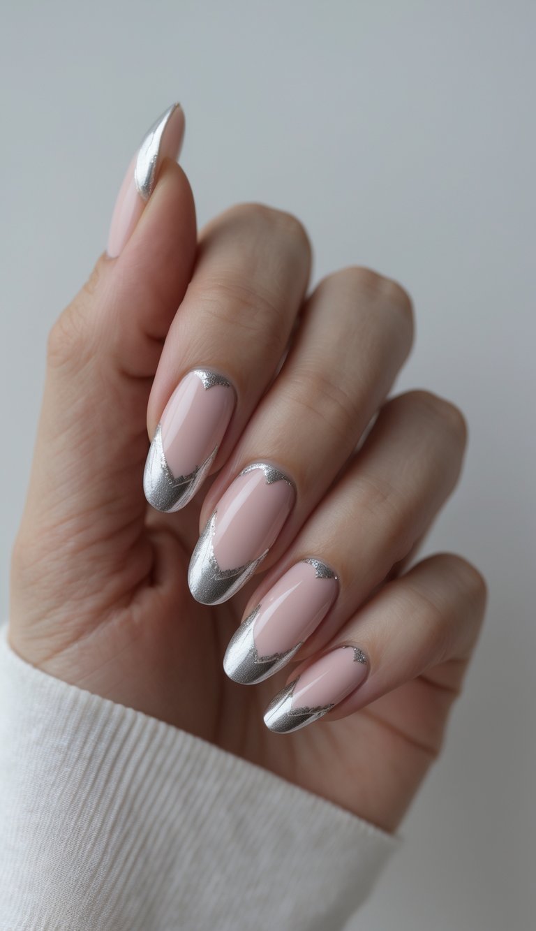Seen from an angled view, a hand shows long almond nails styled in a pink and silver nail art idea, featuring blush-pink bases with curved silver chrome detailing.