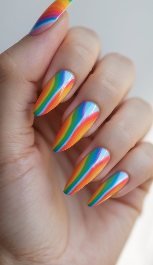A close-up of hands featuring an arched rainbow nail art idea with multicolored stripes painted precisely over a sky-blue base on long tapered nails.