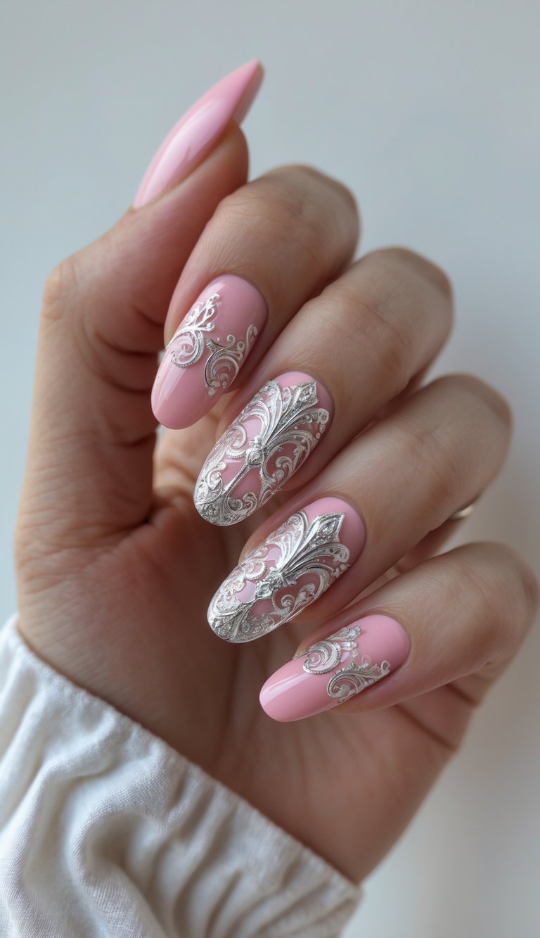Against a soft background, manicured fingers display a pink and silver nail art idea with pale pink polish and ornate silver decorative accents.
