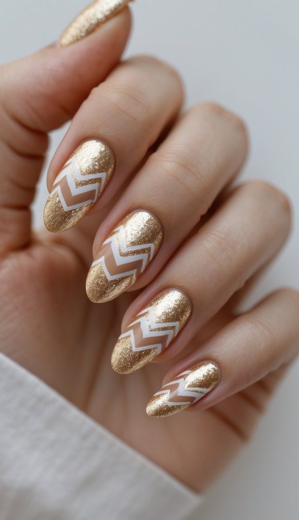 a hand with almond-shaped nails in bright gold glitter polish, with accent nails featuring bold white chevron patterns for a glamorous shimmering nail art idea