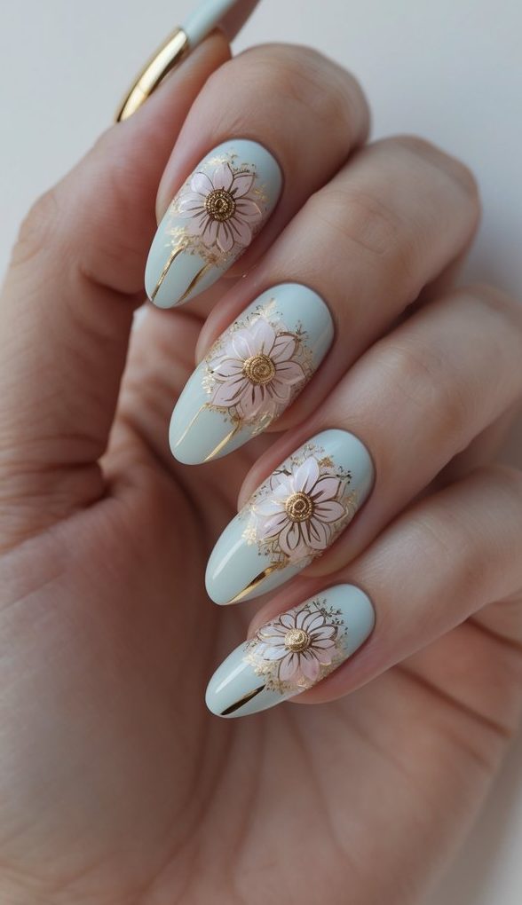 What feels like a luxury manicure shows a hand with pastel blue almond nails, detailed with floral nail art idea elements including pink blossoms, gold foil touches, and thin metallic lines.